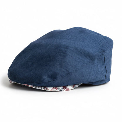 A navy blue textured flat cap in front of a white background, with a red, white, and blue plaid patterned brim visible along the edge.
