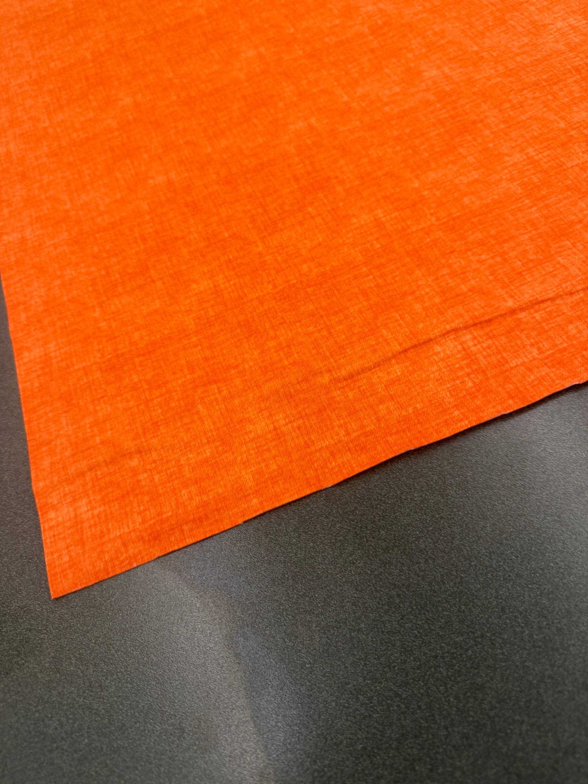 Bright orange cotton fabric or material sample laid diagonally across a dark gray surface.