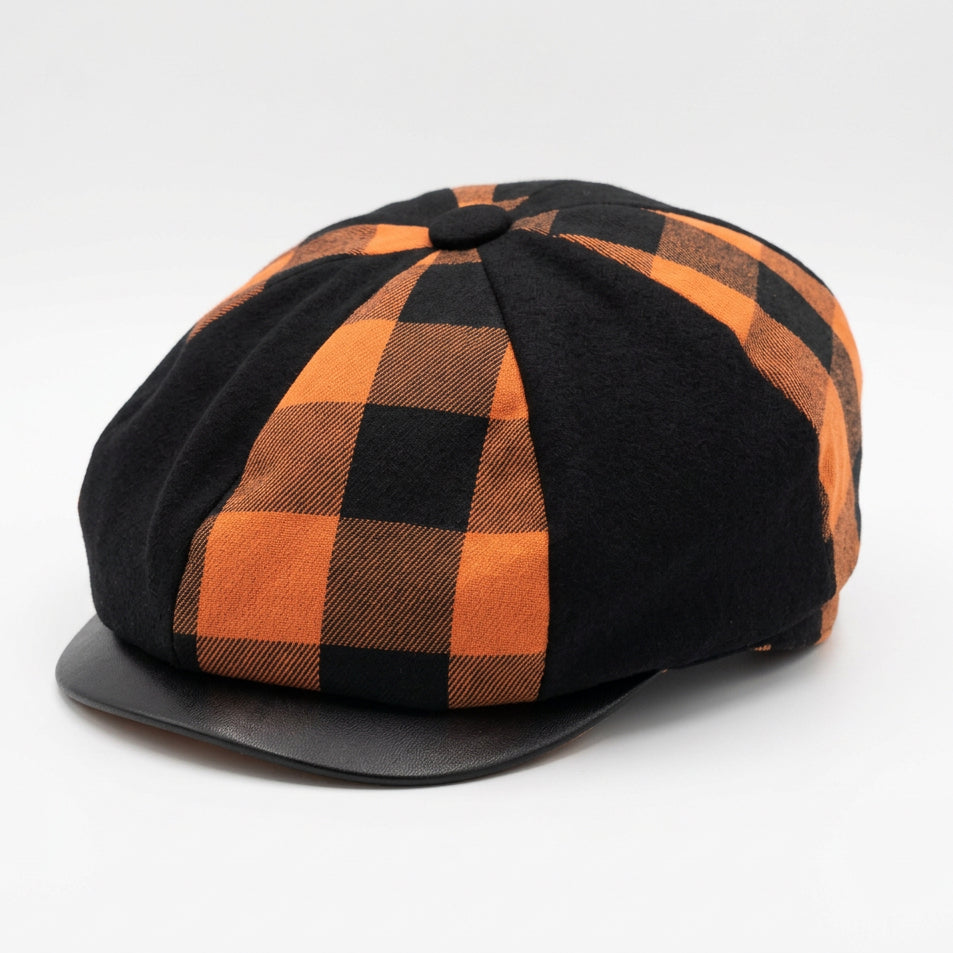 A six-panel flat cap hat with alternating black and orange buffalo plaid and solid black panels, on a plain white background 