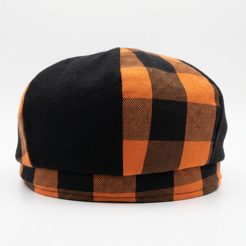 The back of a newsboy style flat cap with alternating orange and black checkered plaid and solid black panels on a solid white background