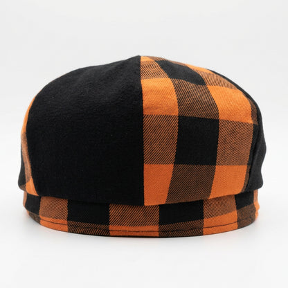 The back of a newsboy style flat cap with alternating orange and black checkered plaid and solid black panels on a solid white background