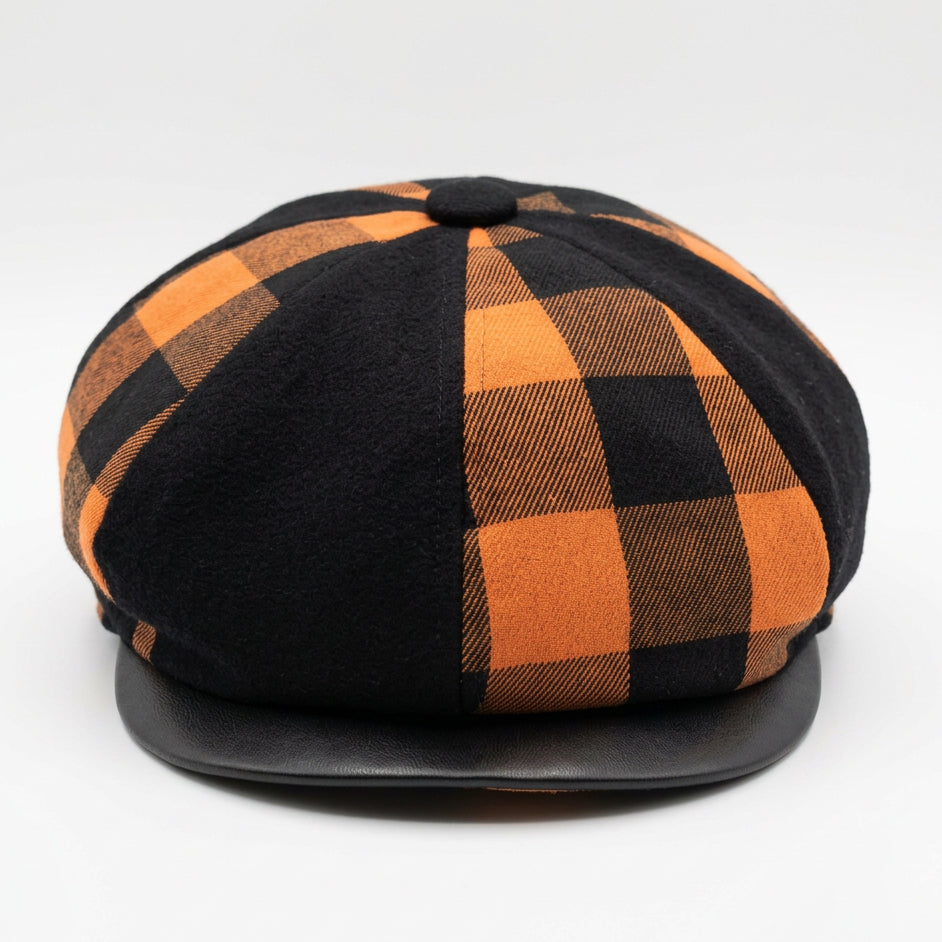 The front of a newsboy style flat cap with alternating orang and black checkered and solid black panels on a solid white background