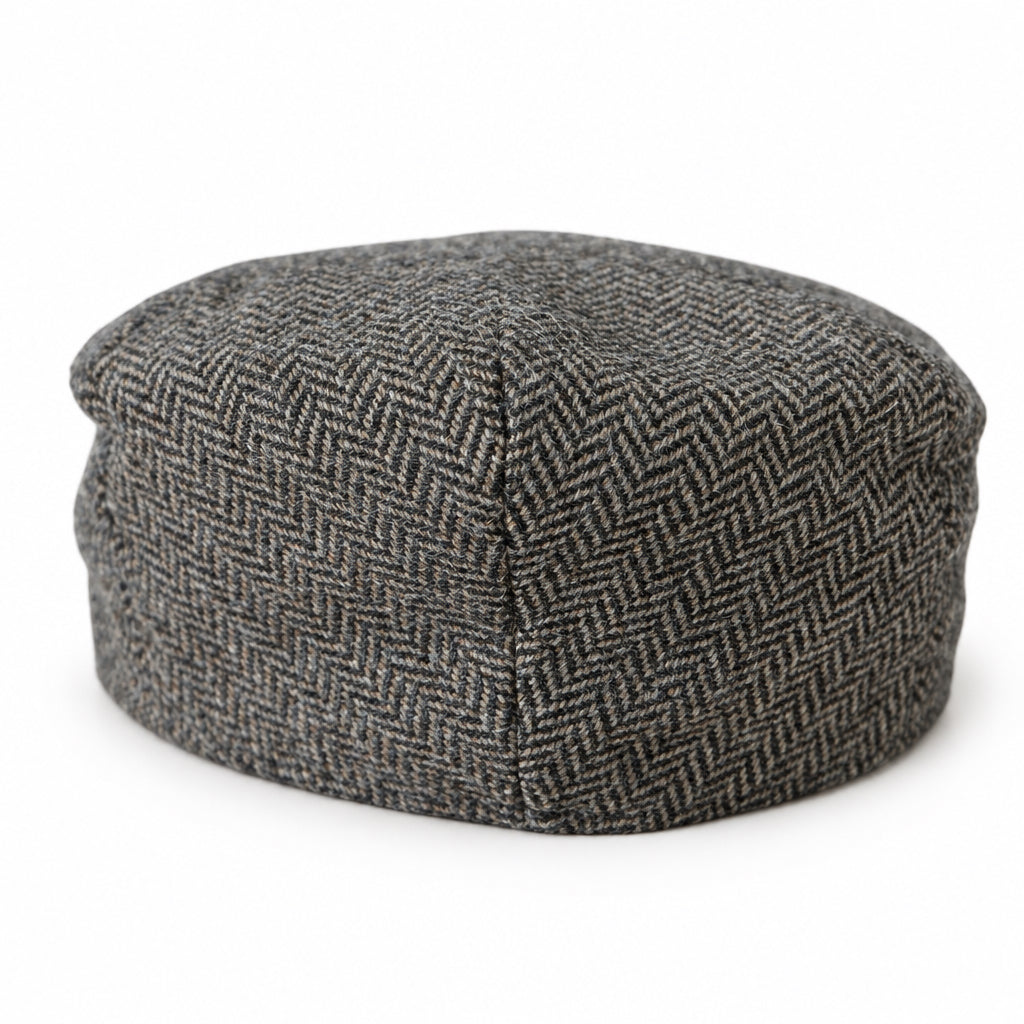 The back side of a brown herringbone tweed flat cap on a solid white background 