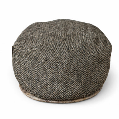 A brown herringbone tweed flat cap resting with a light contrasting brim on a solid white background 