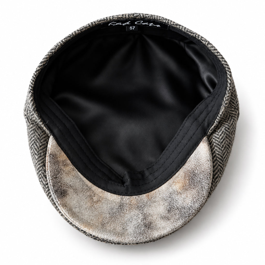 A top-down view of a flat cap with a brown herringbone pattern on the crown and a distressed beige and brown pattern on the visor, set against a solid white background.