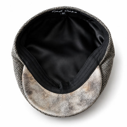 A top-down view of a flat cap with a brown herringbone pattern on the crown and a distressed beige and brown pattern on the visor, set against a solid white background.