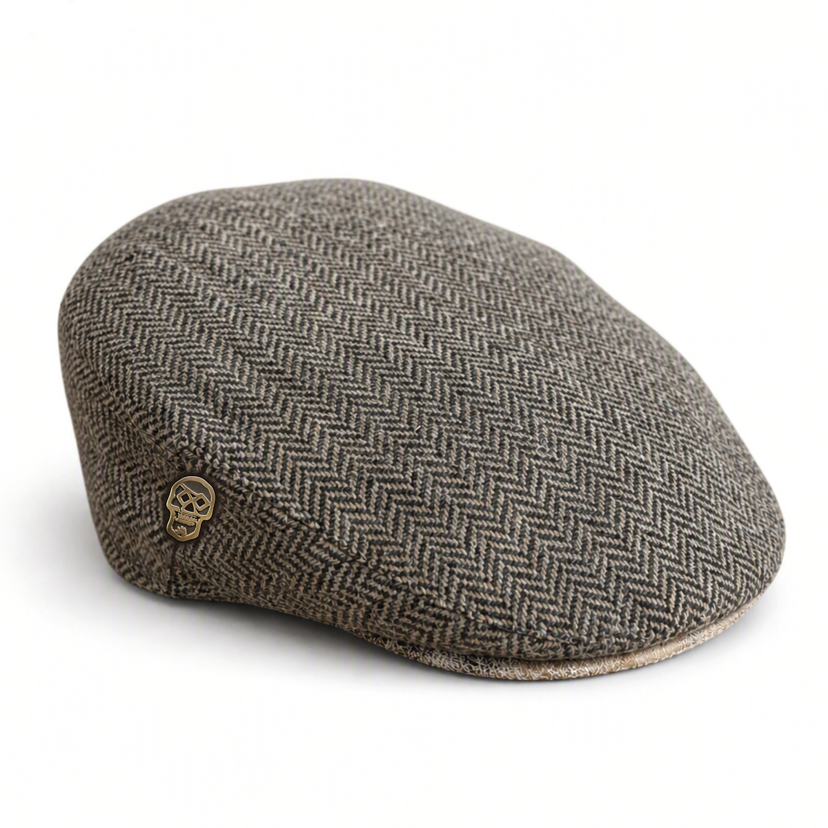 Brown herringbone flat cap with a skull pin on the side and a distressed cream suede brim on a solid white background 
